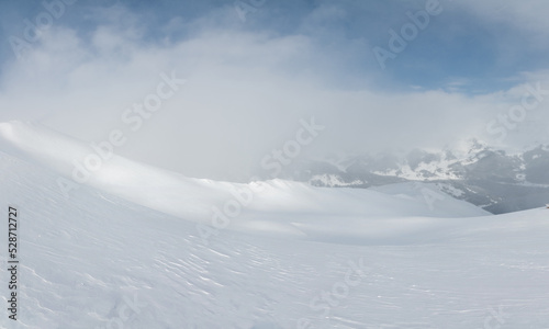 Winter landscape with fog in the mountains and blue sky. View from the top of the snowy mountain and snow field