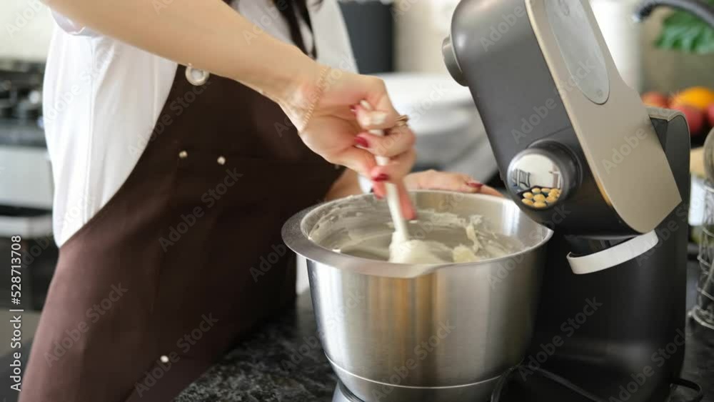 Young Caucasian woman cooks desserts in kitchen at home, process of cooking of cream for cupcakes. Concept of small home business and entrepreneurship. Young Caucasian woman cooks desserts in kitchen at home, process of cooking of cream for cupcakes. Concept of small home business and entrepreneurship.