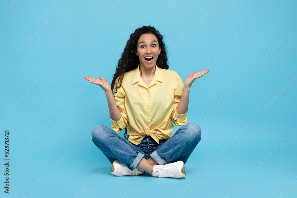 Puzzled excited young woman shrugging shoulders and smiling at camera on blue studio background, full length Puzzled excited young woman shrugging shoulders and smiling at camera on blue studio background, full length