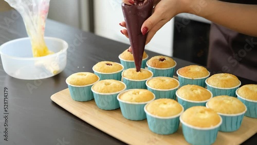 Young Caucasian woman cooks desserts in kitchen at home, process of cooking of cupcakes, filling with sweet filling, jam. Concept of small home business and entrepreneurship.