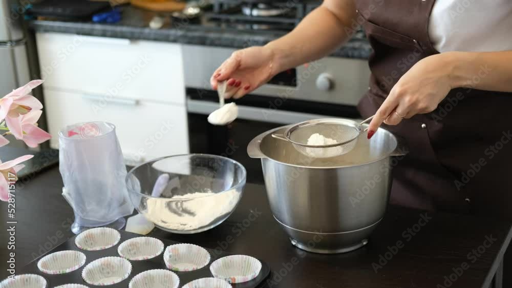 Young Caucasian woman cooks desserts in kitchen at home, process of making dough, sifting flour through a sieve. Concept of small home business and entrepreneurship. Young Caucasian woman cooks desserts in kitchen at home, process of making dough, sifting flour through a sieve. Concept of small home business and entrepreneurship.