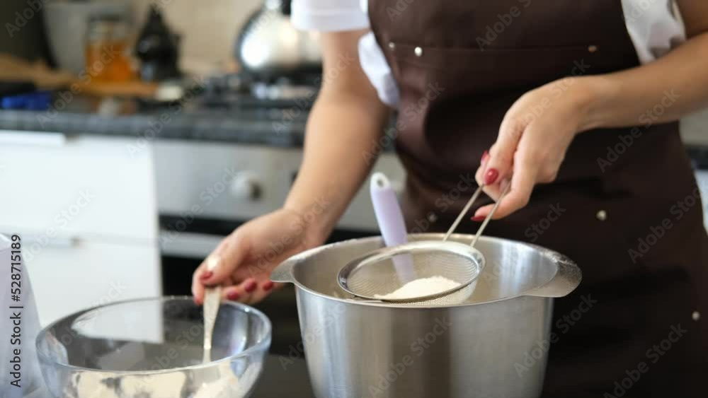Young Caucasian woman cooks desserts in kitchen at home, process of making dough, sifting flour through a sieve. Concept of small home business and entrepreneurship. Young Caucasian woman cooks desserts in kitchen at home, process of making dough, sifting flour through a sieve. Concept of small home business and entrepreneurship.