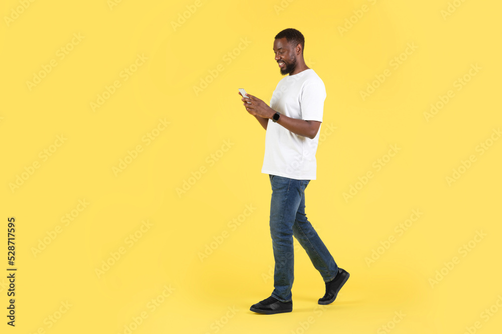 African American Guy Using Cellphone Texting Walking Over Yellow Background African American Guy Using Cellphone Texting Walking Over Yellow Background