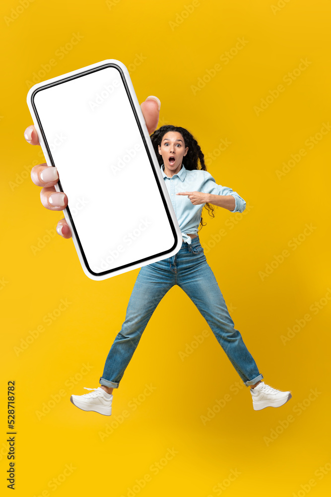 Shocked Arabic Lady Showing Phone Screen Over Yellow Background, Vertical Shocked Arabic Lady Showing Phone Screen Over Yellow Background, Vertical