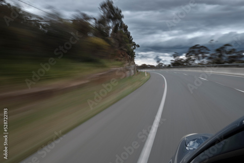 Traveling down a highway at speed approaching a bend. Tree lined highway under a dramatic cloudy sky. Diminishing perspective towards a curve in the road