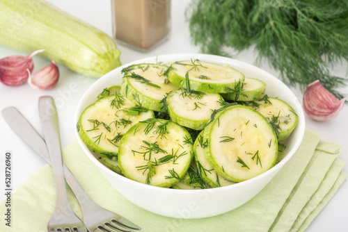 Fast pickled zucchini with garlic and dill in white bowl on green napkin. Homemade vegetable marinated appetizer.