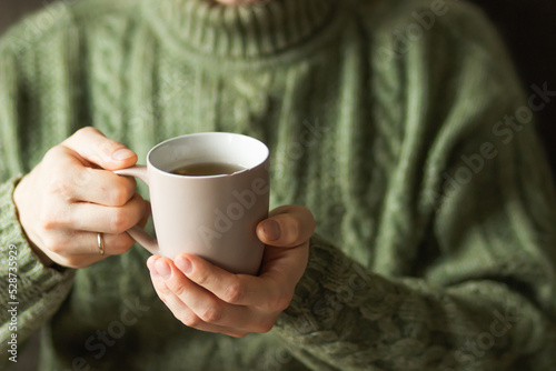 Married man wearing green knitted woolen sweater holding hot cup of tea in the cold autumn or winter morning.