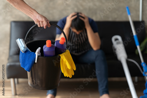 Cleaning service. Bucket with sponges  chemicals bottles and mopping stick. Rubber gloves  plunger and towel. Man standing in his house.