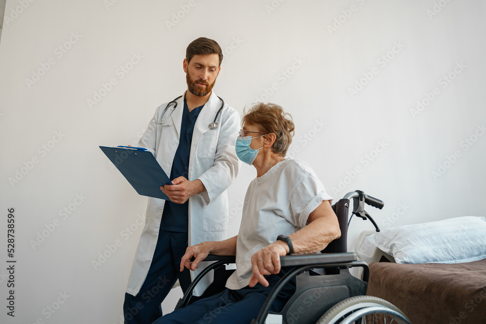 Doctor in mask explaining to a sick patient in wheelchair details of treatment. High quality photo Doctor in mask explaining to a sick patient in wheelchair details of treatment. High quality photo