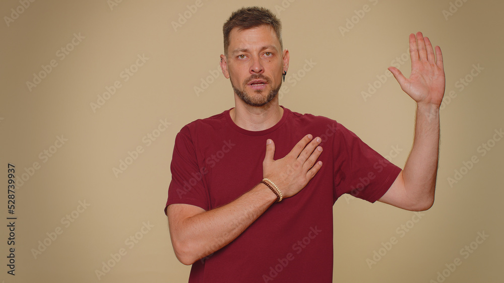 I swear to be honest. Sincere responsible handsome young man raising hand to take oath, promising to be honest and to tell truth, keeping hand on chest. Adult stylish guy isolated on beige background I swear to be honest. Sincere responsible handsome young man raising hand to take oath, promising to be honest and to tell truth, keeping hand on chest. Adult stylish guy isolated on beige background