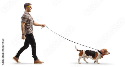 Full length profile shot of a cool young man walking a basset hound dog on a lead