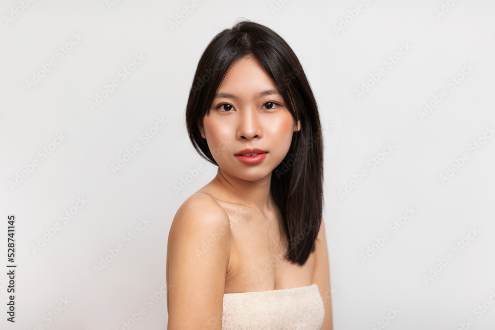 Pretty young korean lady with smooth skin and dark hair standing wrapped in towel over white background Pretty young korean lady with smooth skin and dark hair standing wrapped in towel over white background
