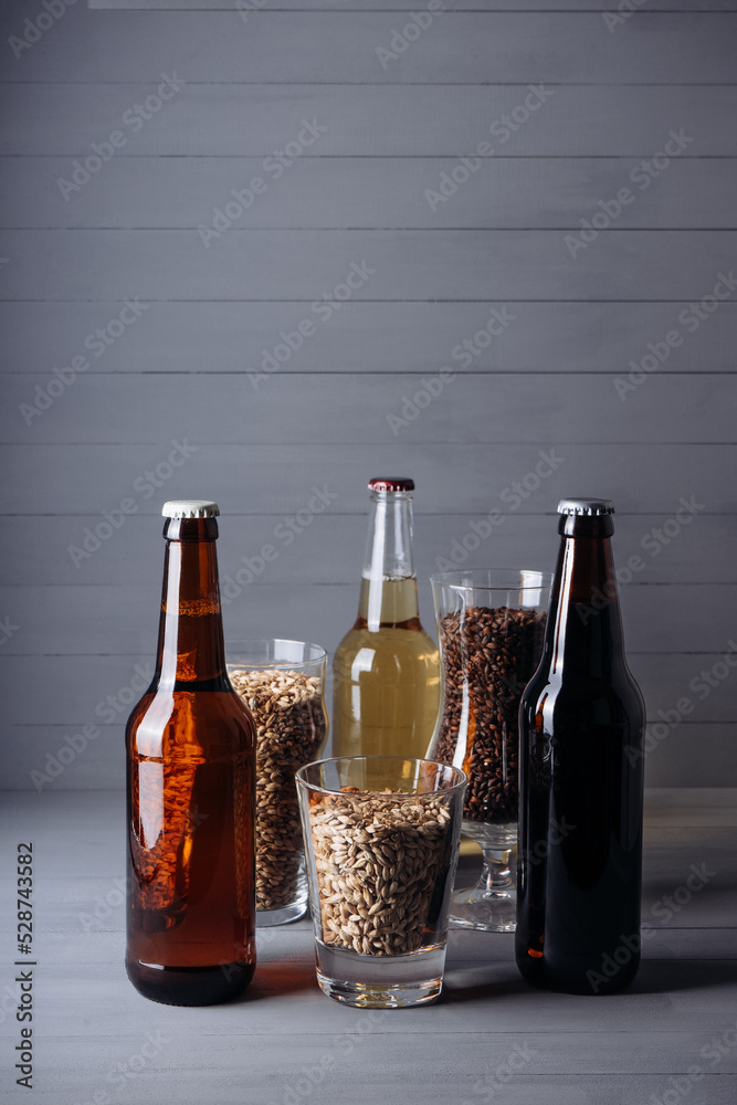 bottles with craft beer  and beer glasses with barley malt on a grey wooden background.  Ale or lager from pilsner malt.  homemade home-brewed beer. - obrazy, fototapety, plakaty 