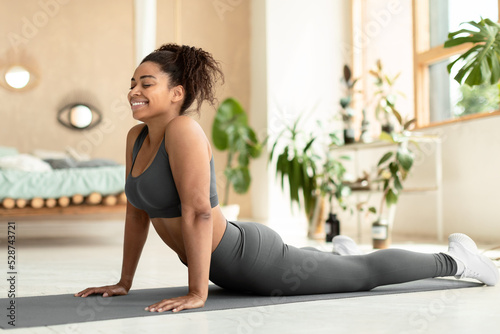 Working out at home. Fit black lady stretching, doing Cobra exercise or standing in upward-facing dog posture