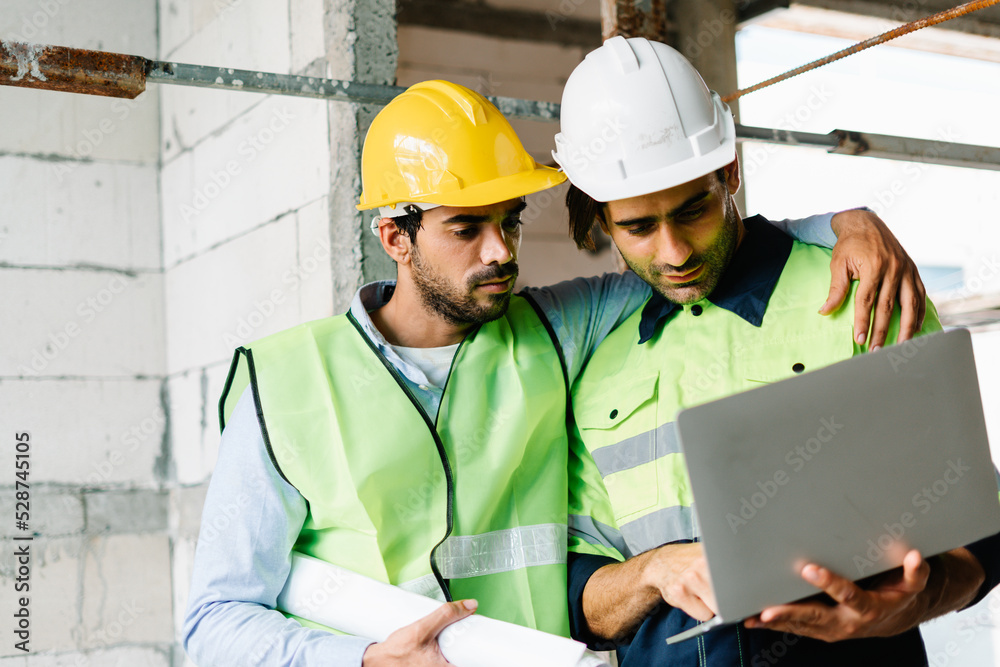 Civil Engineer and Contractor working in vest with safety hardhat looking at laptop computer while working on construction site Civil Engineer and Contractor working in vest with safety hardhat looking at laptop computer while working on construction site