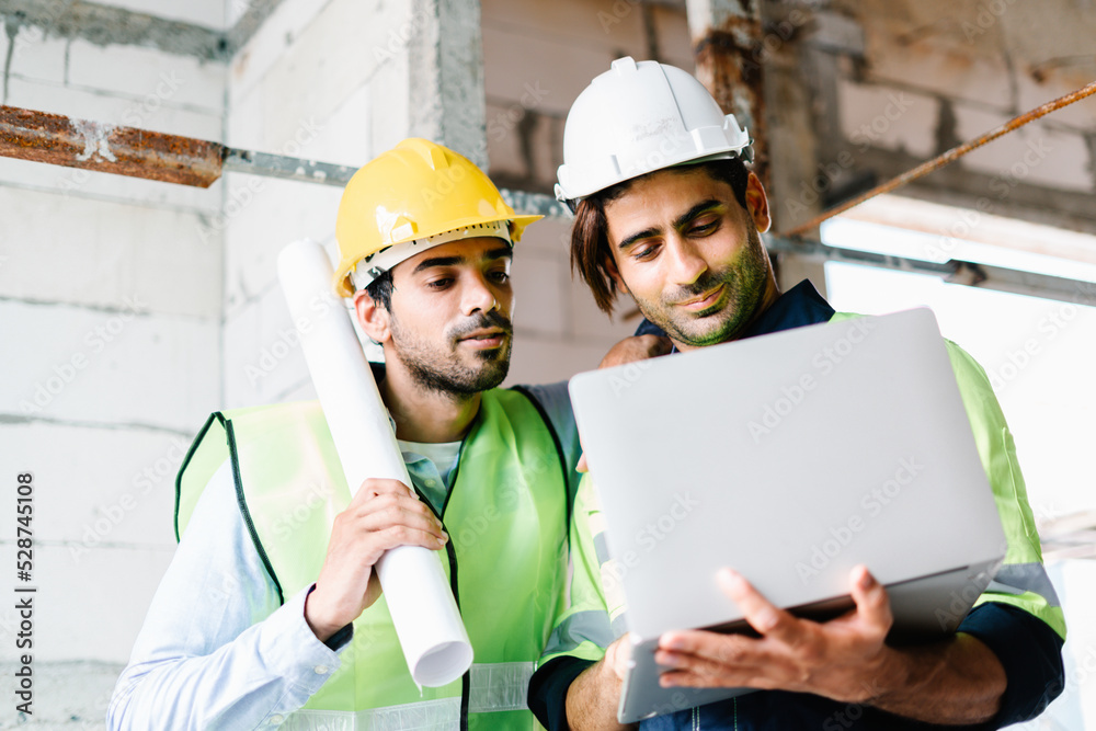 Civil Engineer and Contractor working in vest with safety hardhat using laptop computer while standing and working together on construction site Civil Engineer and Contractor working in vest with safety hardhat using laptop computer while standing and working together on construction site