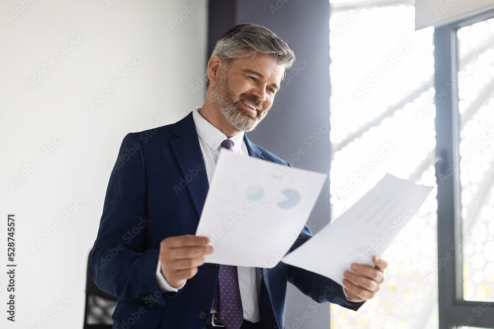 Happy Middle Aged Entrepreneur Reading Business Papers At Office Happy Middle Aged Entrepreneur Reading Business Papers At Office