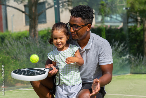 Black father teaching daughter to play paddle tennis 