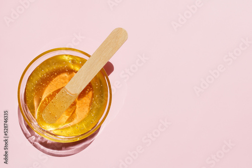 Liquid yellow sugar paste, wooden spatula on a pink background. Removing unwanted hair. Sugaring. Depilation. Epilation. Beauty. Top view. Place for text.