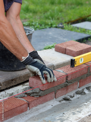 Construction work in progress. Male builder working with red bricks. Masonry wall close up photo. 
