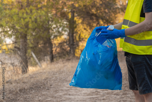 Detalle de hombre guardabosque caucásico, metiendo botella de plástico en bolsa de basura en la montaña. Fotografía horizontal con espacio para texto.