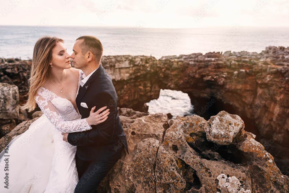 bride and groom sit on rocks and close their eyes. ocean view. c