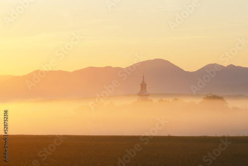 Church of Pribovce village shrouded in morning fog, Slovakia.