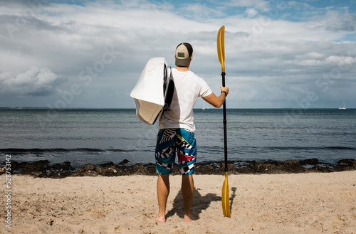 man stood looking at the sea holding a kayak ready to explore