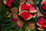 Ripe sweet watermelon slices on plates. Around the leaves of wild grapes and hops. View from above. Family dinner. Dessert. Rustic.