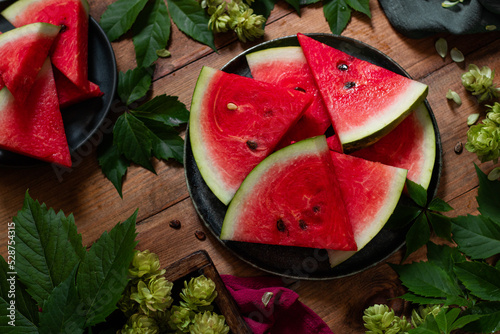 Ripe sweet watermelon slices on plates. Around the leaves of wild grapes and hops. Yop view. Family dinner. Dessert. Country style. Rustic. photo