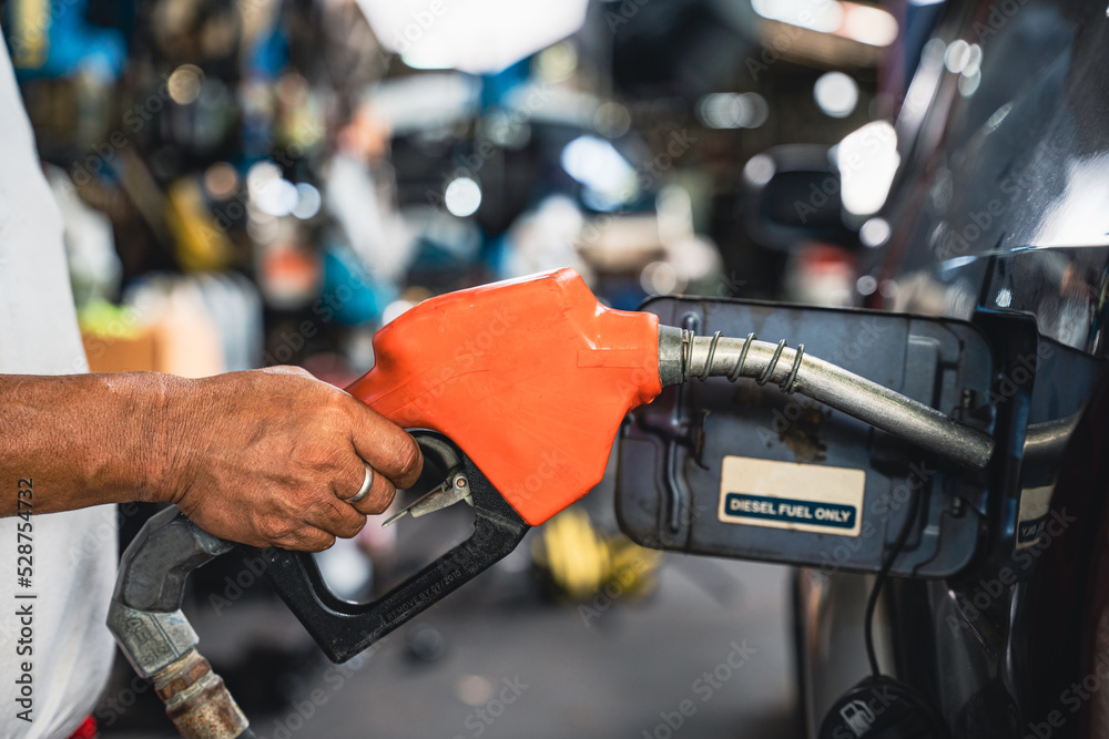 Worker holding a fuel injector is refueling a car. Worker holding a fuel injector is refueling a car.