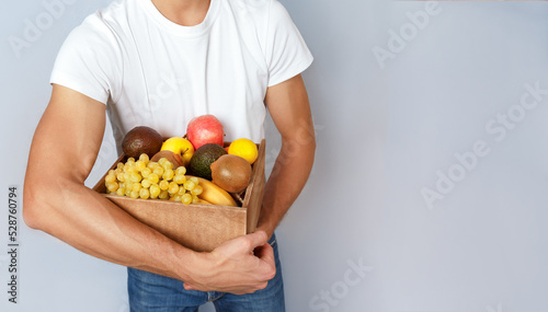 A man is holding a paper bag with vegetables and fruits.