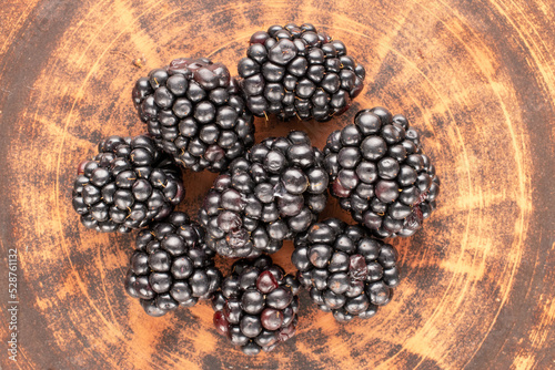 Several sweet blackberries on a clay dish, close-up, top view.