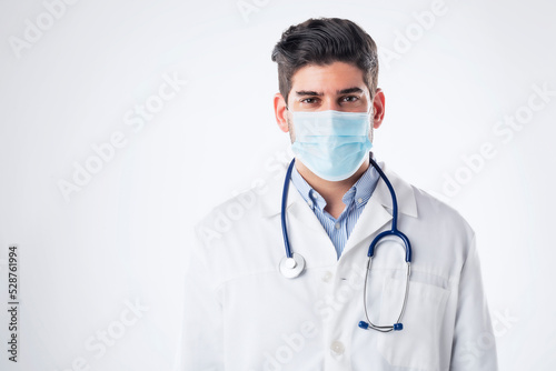 Malde doctor wearing surgical face mask while standing at isolated white background