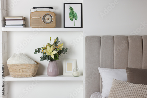 Stylish vase with flowers, retro radio and decor on shelves indoors. Bedroom interior elements