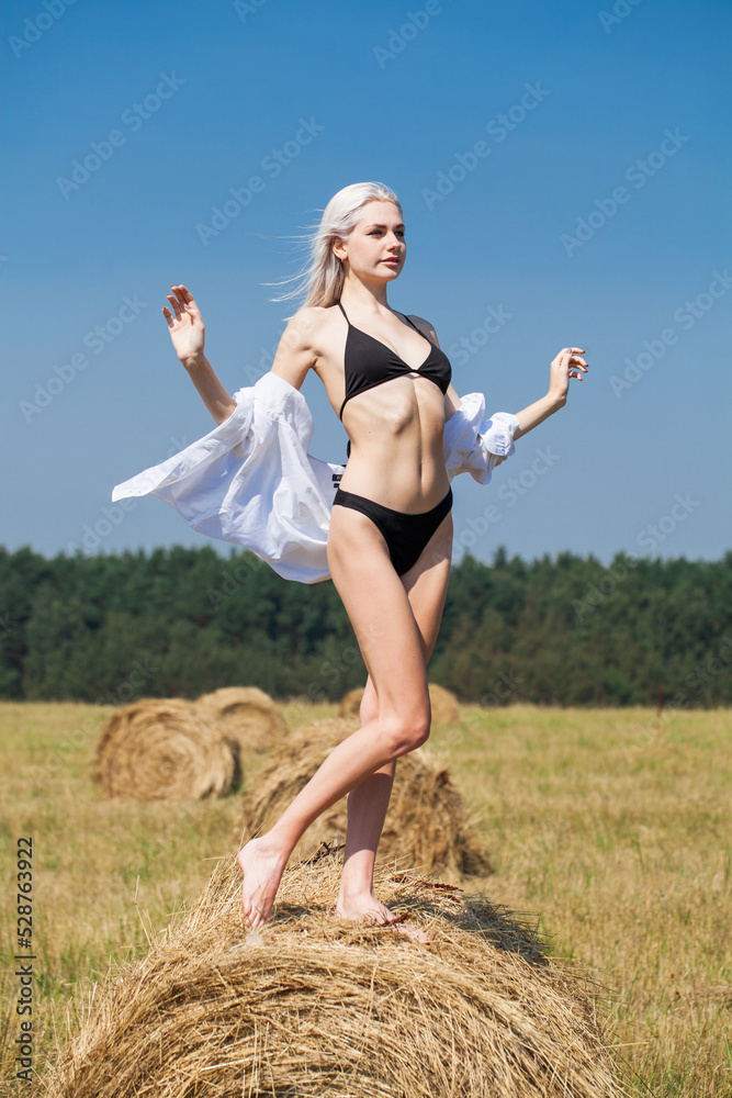 Sexy blonde woman in black bikini and white shirt posing on a haystack Sexy blonde woman in black bikini and white shirt posing on a haystack
