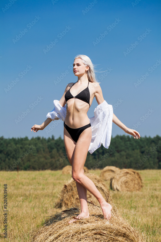 Sexy blonde woman in black bikini and white shirt posing on a haystack Sexy blonde woman in black bikini and white shirt posing on a haystack