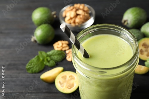 Fresh feijoa smoothie in glass on black wooden table, closeup
