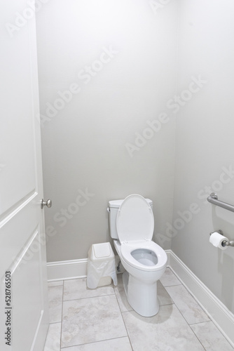 A small half bathroom with gray walls and a toilet with tile floors in a new construction house with a handicap railing