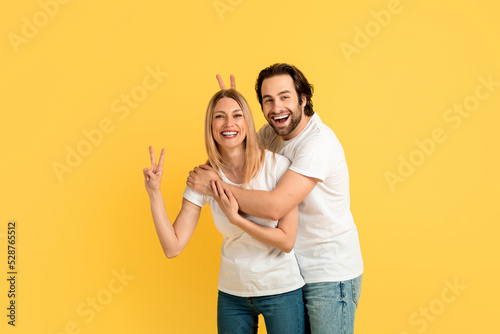 Cheerful funny millennial caucasian woman and man in white t-shirts have fun, show peace sign with hands © Prostock-studio