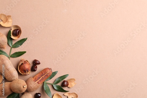 Ripe tamarinds and fresh leaves on beige background, flat lay. Space for text