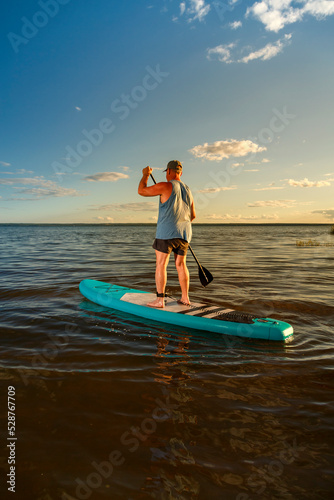 a man in shorts stands with a paddle on a SUP board at sunset in the lake. © finist_4