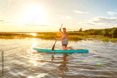 a man in shorts sits on a sup board at sunset in the water. © finist_4