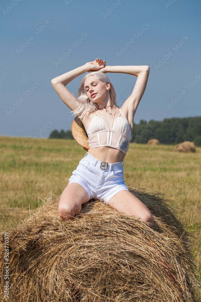 Young beautiful blonde girl in a straw hat posing in the hayloft Young beautiful blonde girl in a straw hat posing in the hayloft