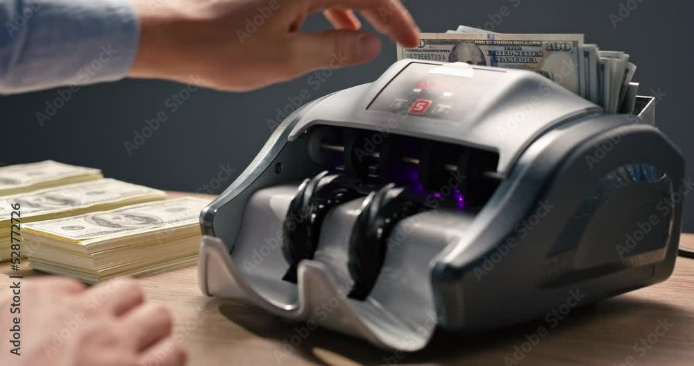 Close up of currency counting machine counting dollar banknotes. Banking and finance business. Male hand putting cash money in bank automatic equipment and pressing button. Financial concept