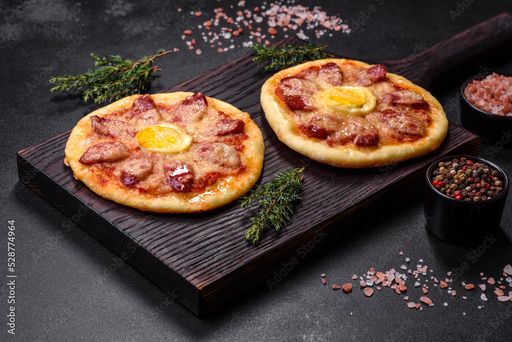 Homemade pizza with sausages, tomatoes, cheese, spices and herbs on a wooden cutting board