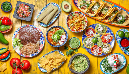 Mexican festive food for independence day independencia - chiles en nogada, tacos al pastor, chalupas pozole, tamales, chicken with mole poblano sauce. Yellow background.