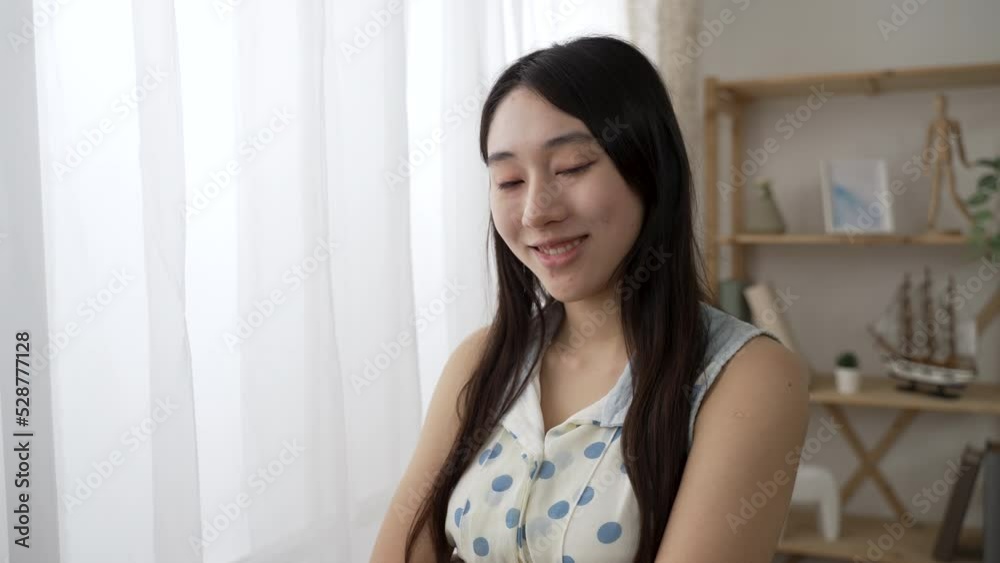 shoulder shot portrait of an attractive Asian woman turning to look at the camera with smile near the window at home during the day.