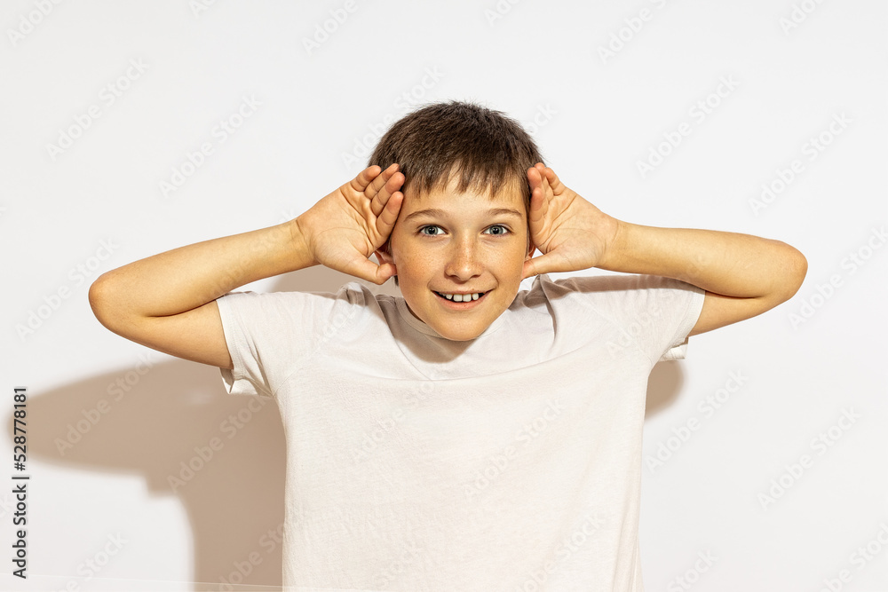 smiling boy, teasing, putting his palms to his ears. on a white background. smiling boy, teasing, putting his palms to his ears. on a white background.