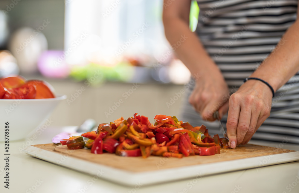 Close-up of a woman cutting Bell Pepper with a kitchen knife in a bright kitchen.